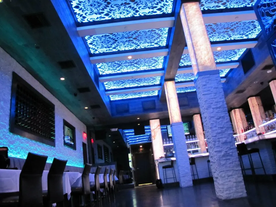 A bar and restaurant with blue-lit decorative ceiling panels and stone-clad columns.
