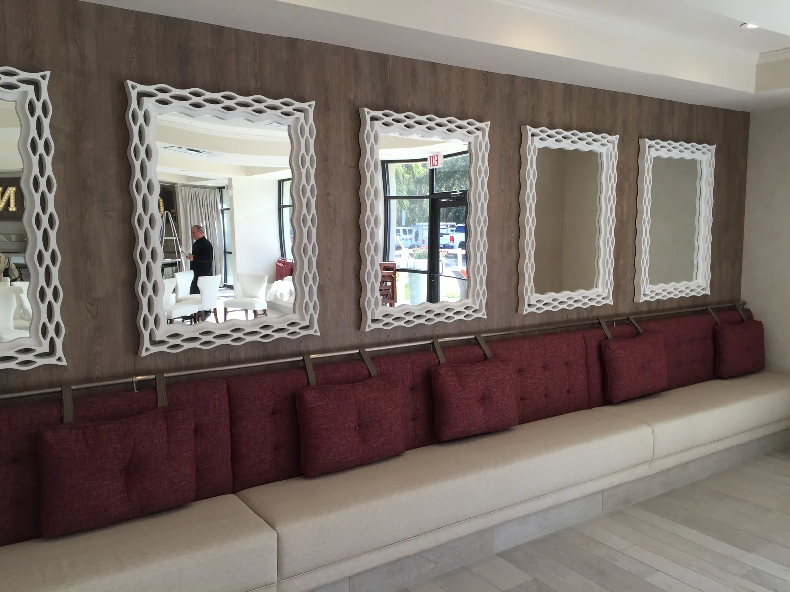 A finished interior: a long upholstered banquette with red cushions under a row of white framed mirrors.